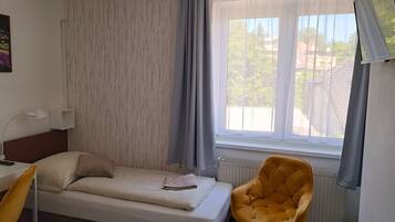 Un lit simple avec une tête de lit, une table de chevet avec une lampe, une chaise et une fenêtre avec des rideaux.