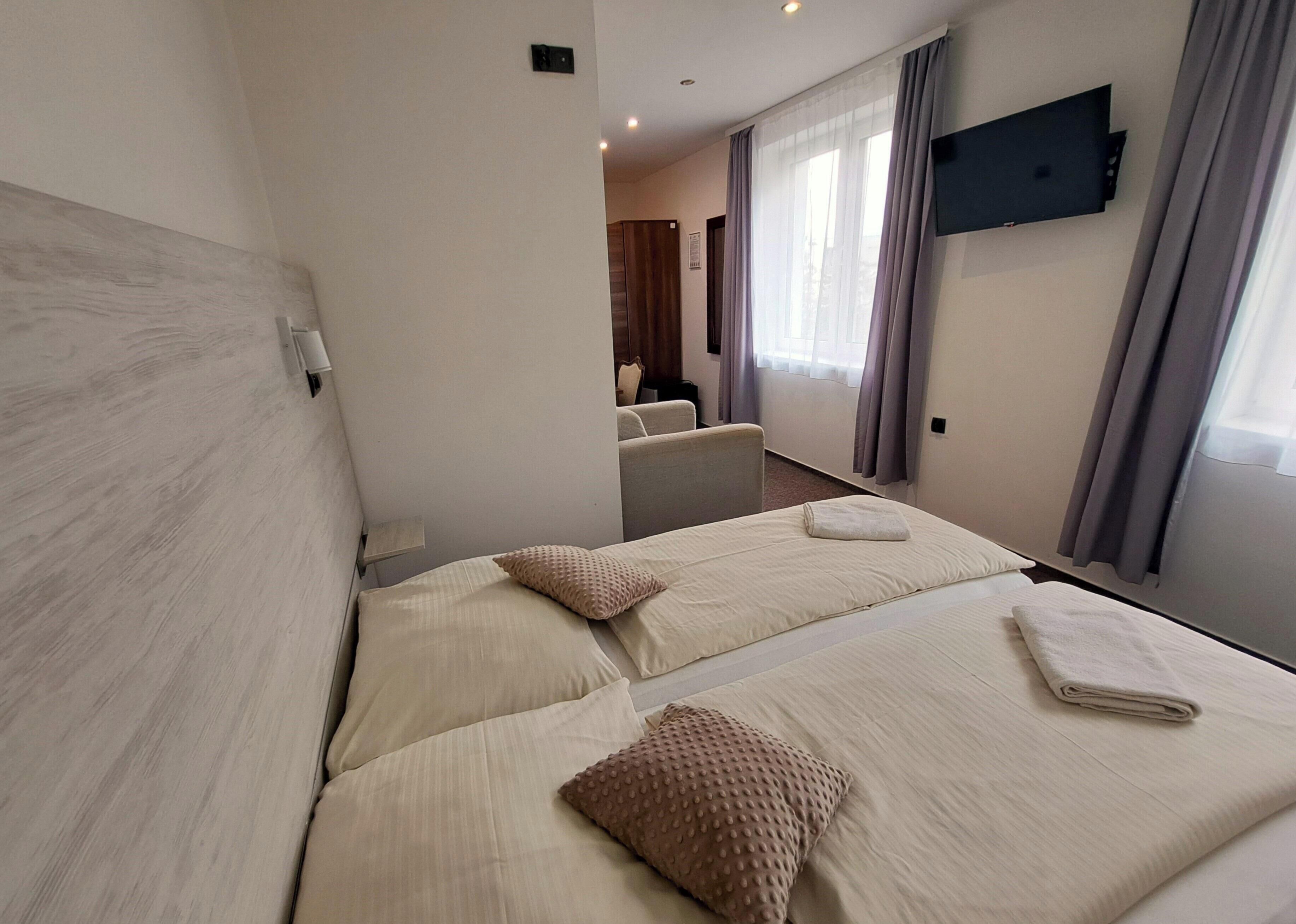 Habitación de hotel con dos camas, un televisor montado en la pared y vista hacia la habitación contigua.