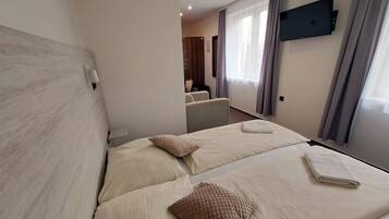Habitación de hotel con dos camas, un televisor montado en la pared y vista hacia la habitación contigua.