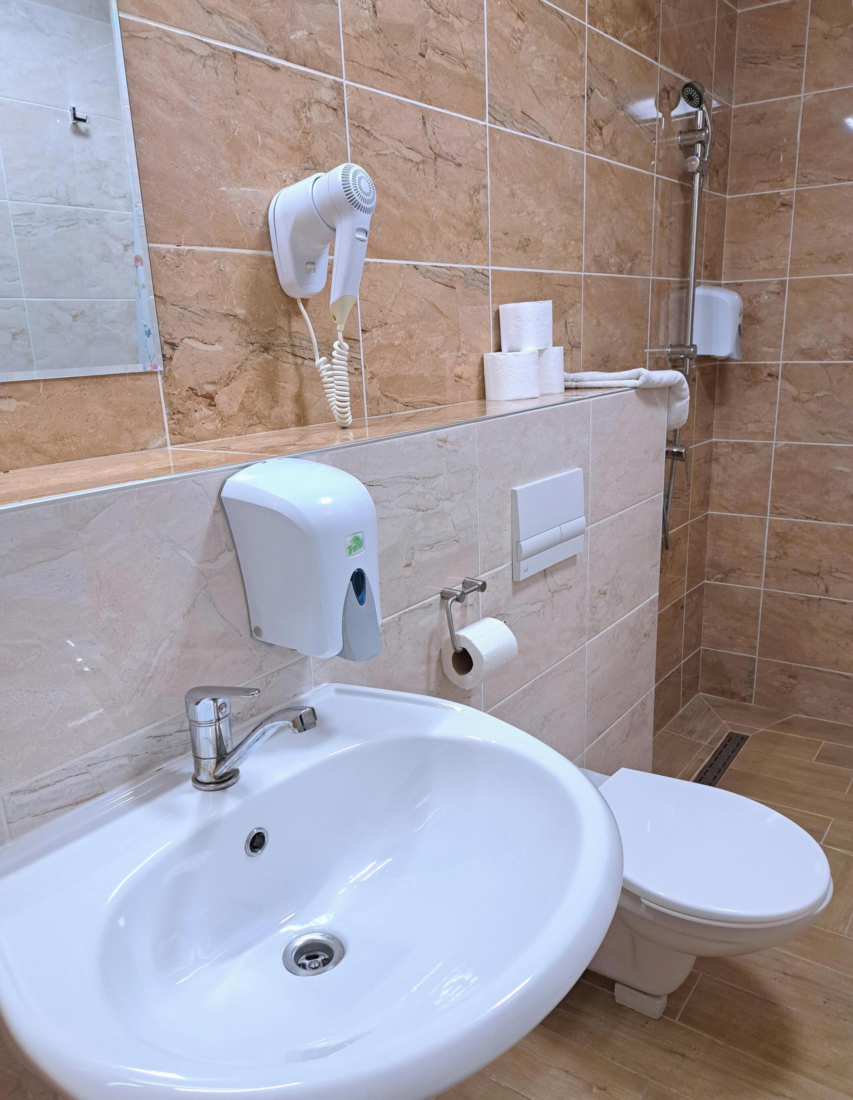 A bathroom with a sink, toilet, hairdryer, and hand dryer.