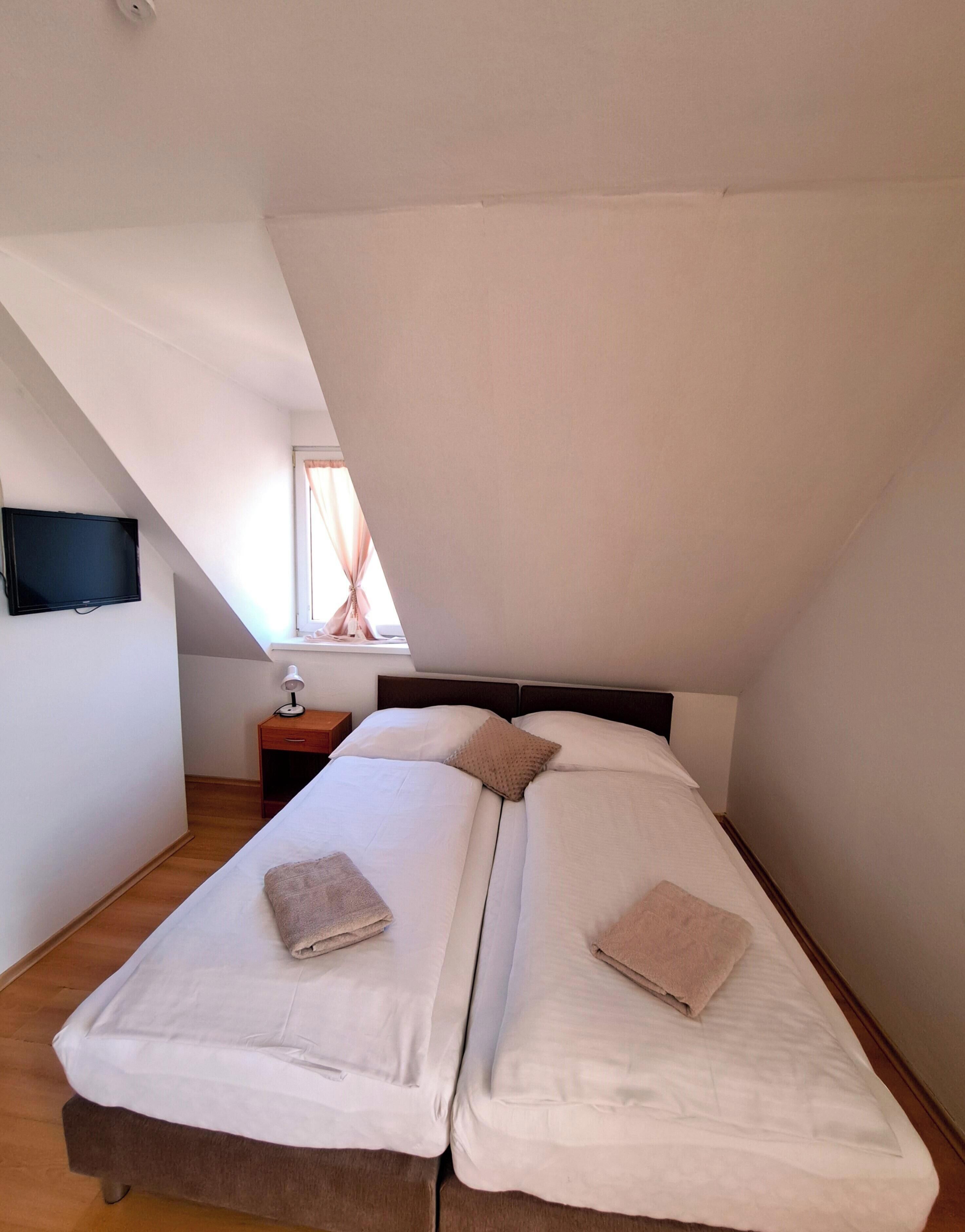 A bedroom with two beds, a nightstand, a lamp, and a television on the wall.