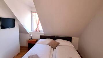 A bedroom with two beds, a nightstand, a lamp, and a television on the wall.