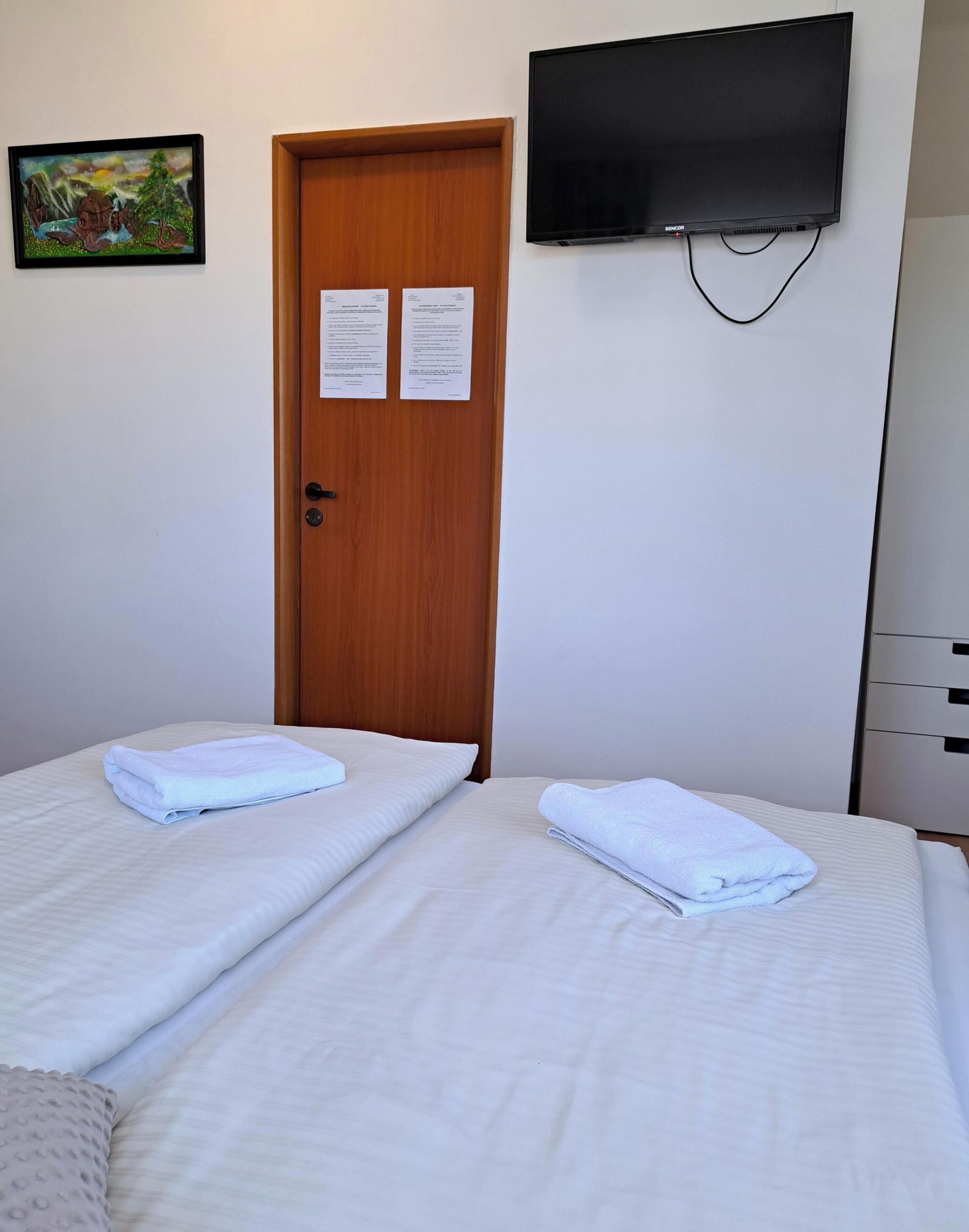 A hotel room with two beds, a wooden door, a television mounted on the wall, and a painting on the wall.