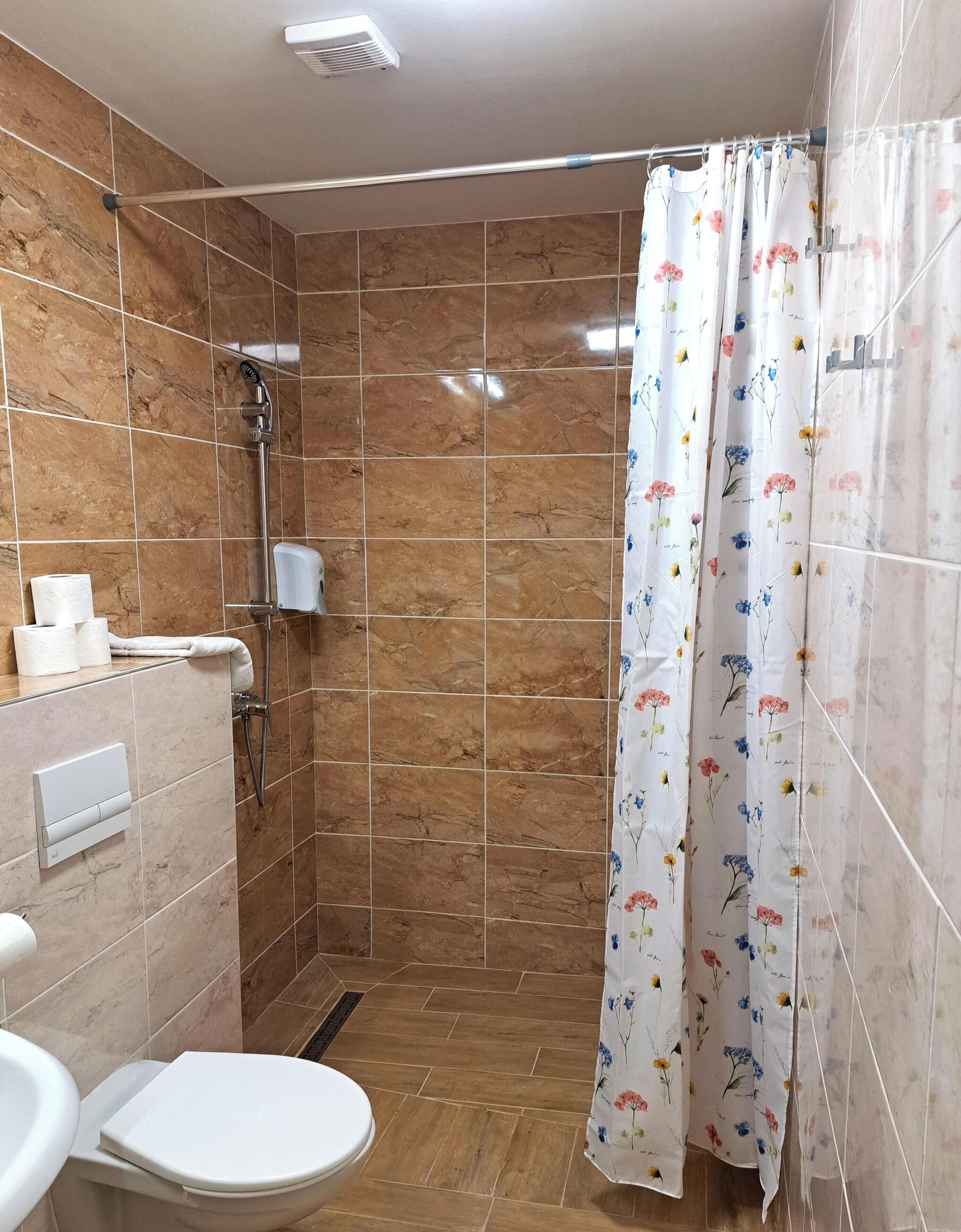 A bathroom with a shower, toilet, and a towel dispenser.