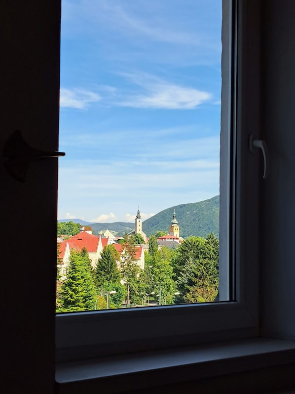 A window view of a town with buildings and a church tower. - Penzión Al Corso (Banska Bystrica)