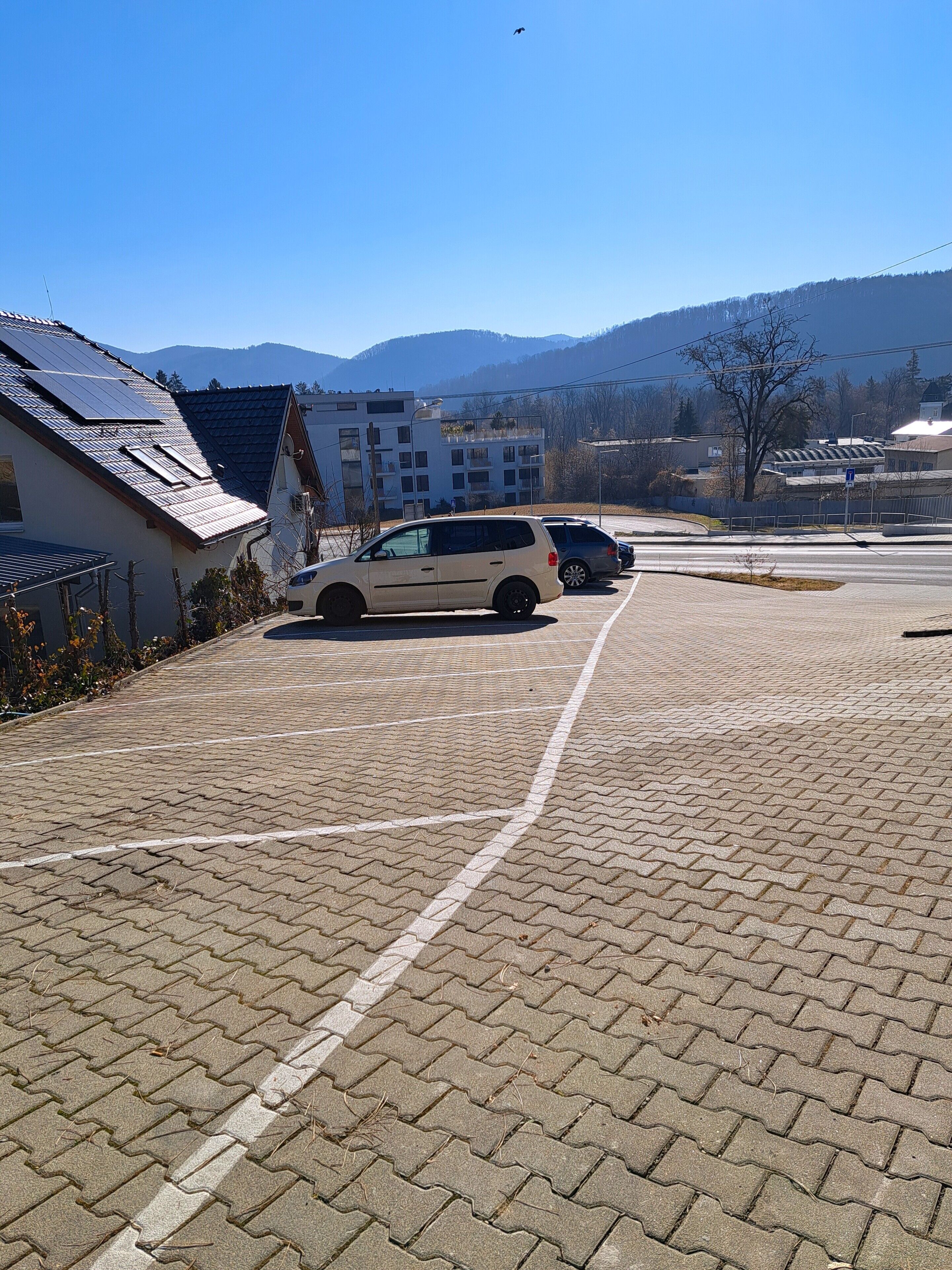 A parking lot with paved ground, a white car, and a building with a sloped roof.