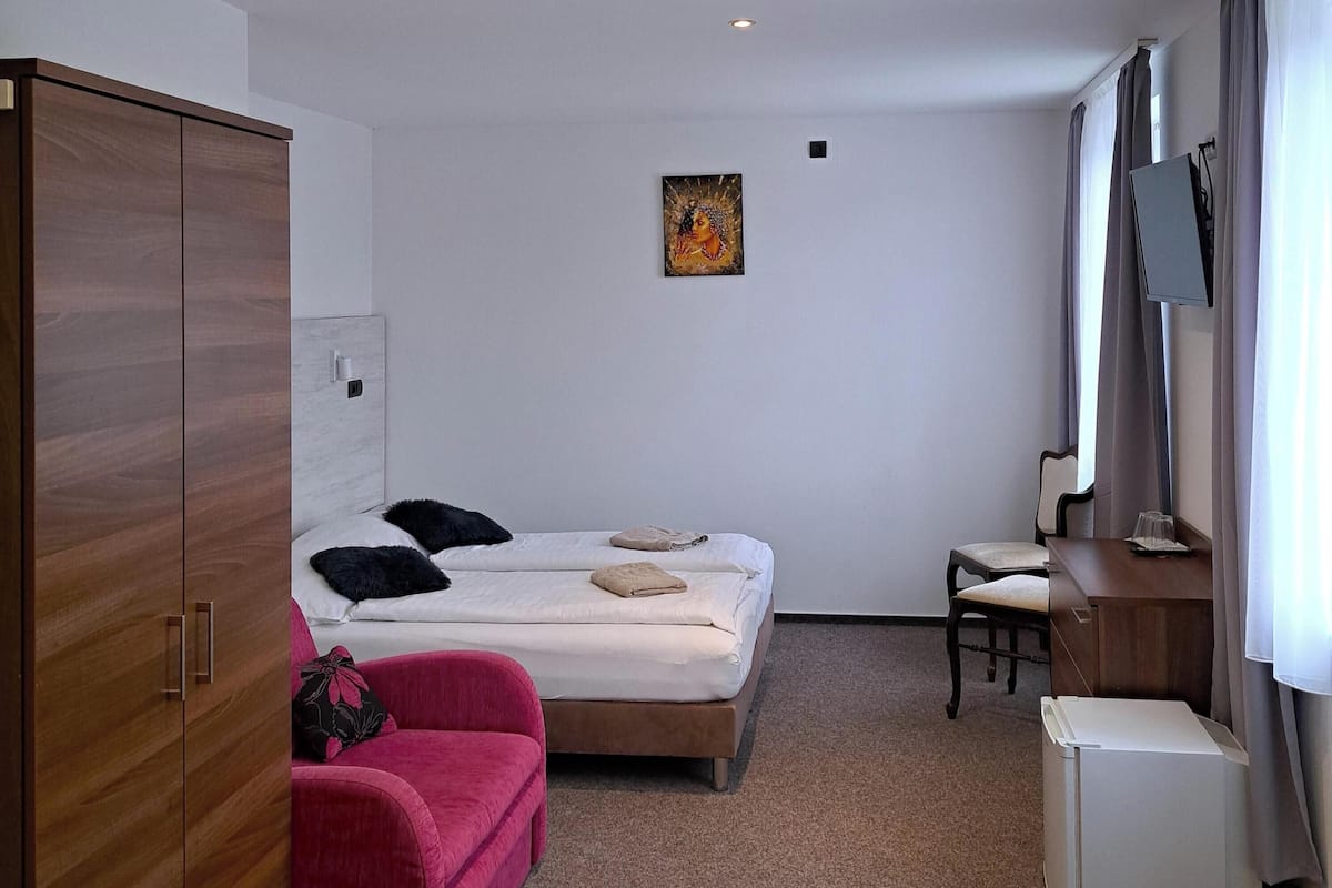 Et hotelværelse med en seng, et skrivebord, et skab og et lille billede på væggen.
