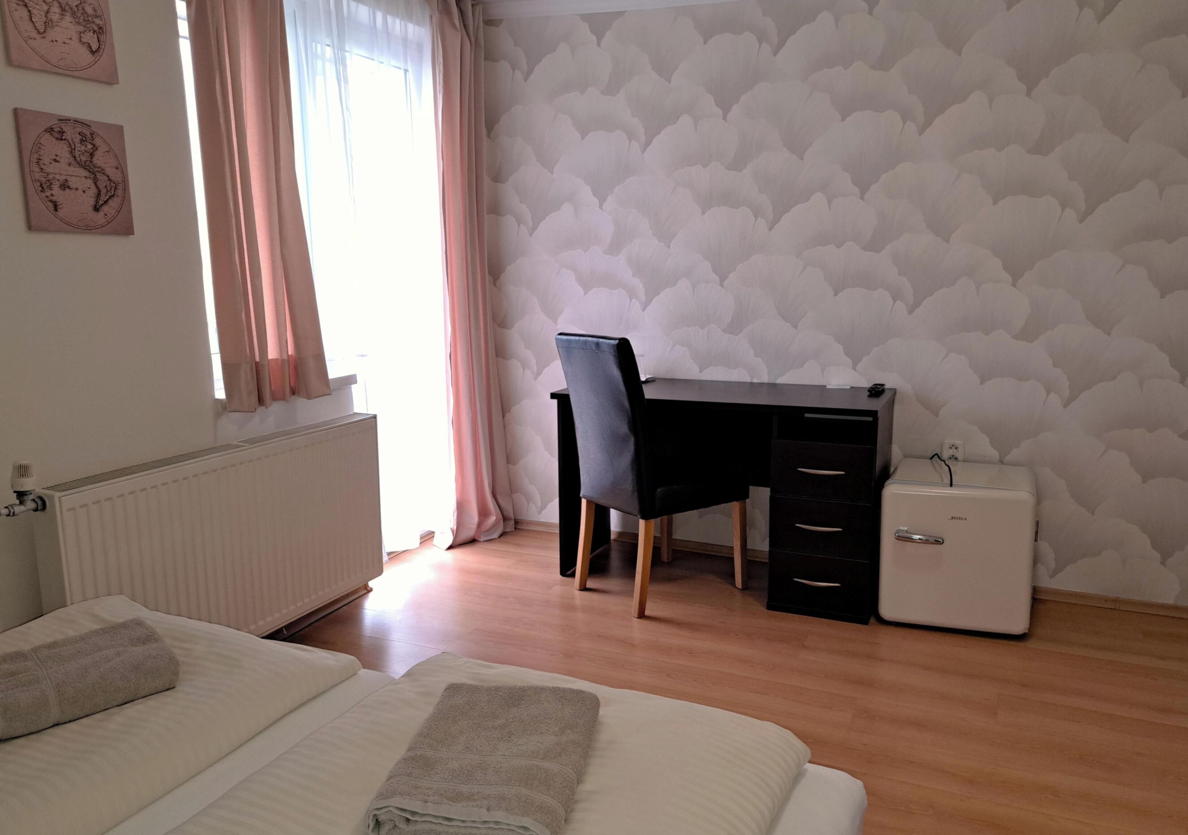 A bedroom with a bed, a desk, a chair, a dresser, and a small white appliance.