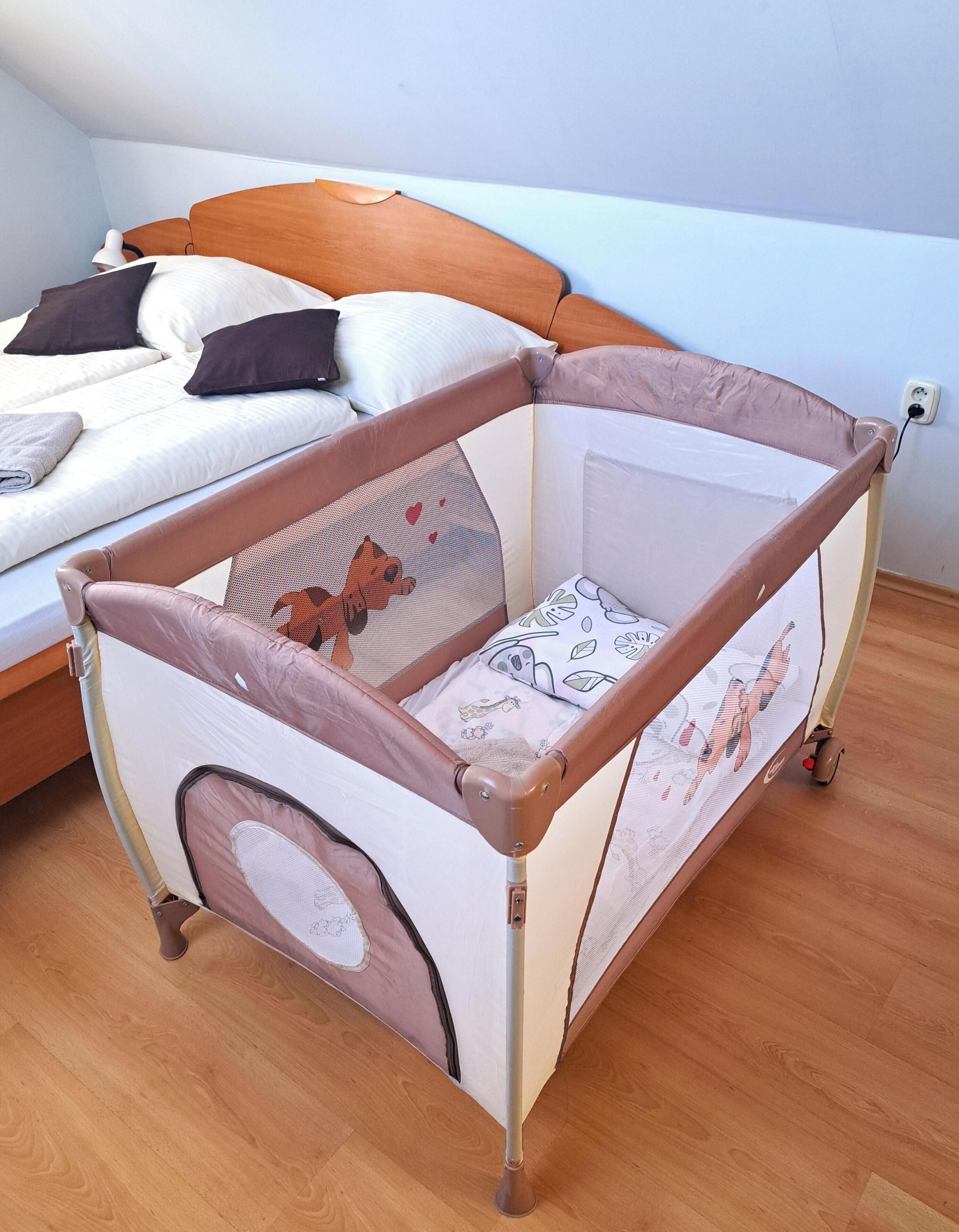 A baby crib with a wooden frame and mesh sides, positioned in a room with a bed and a nightstand.