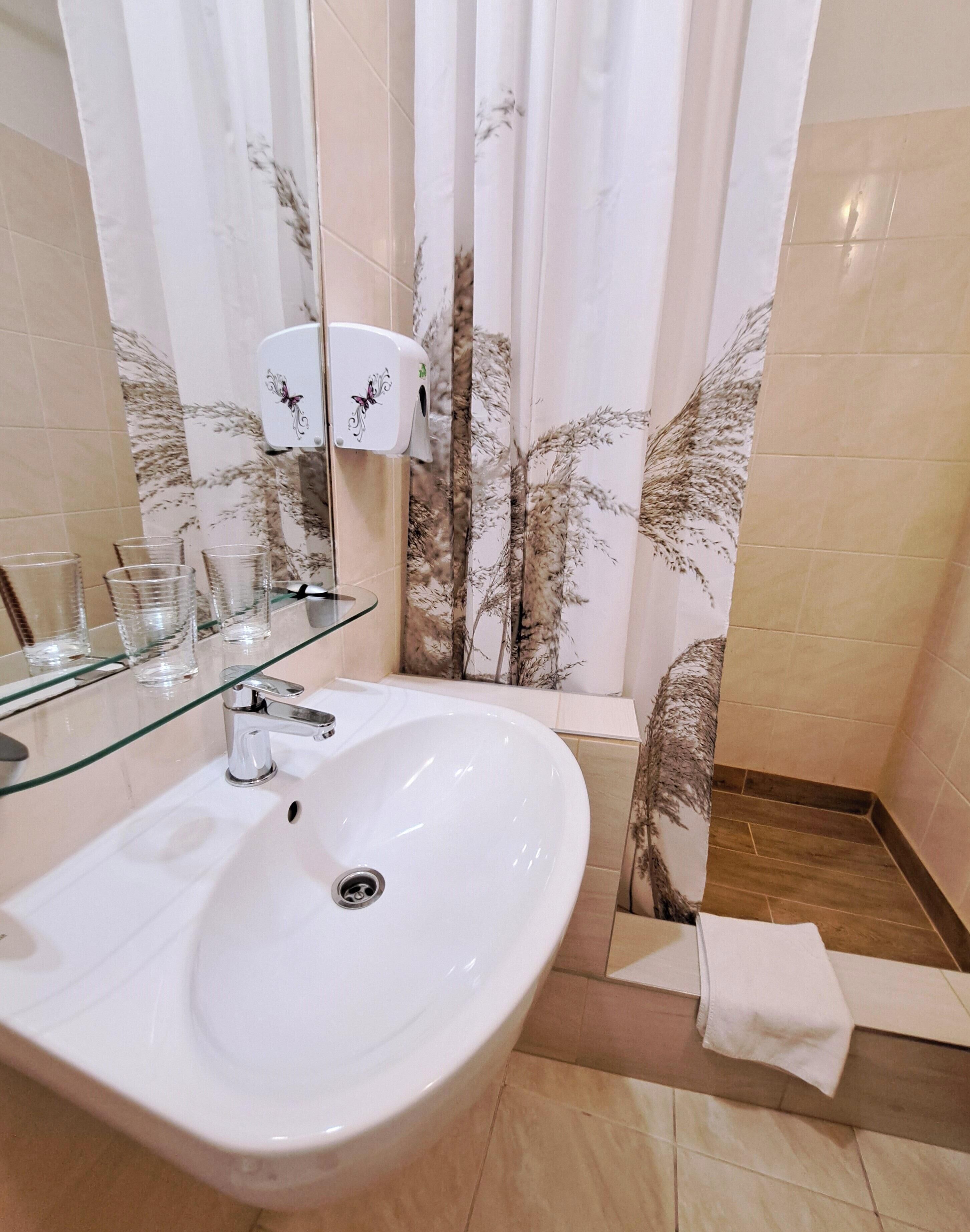 A bathroom with a white sink, glass shelves, a hand dryer, and a shower curtain with a floral pattern.