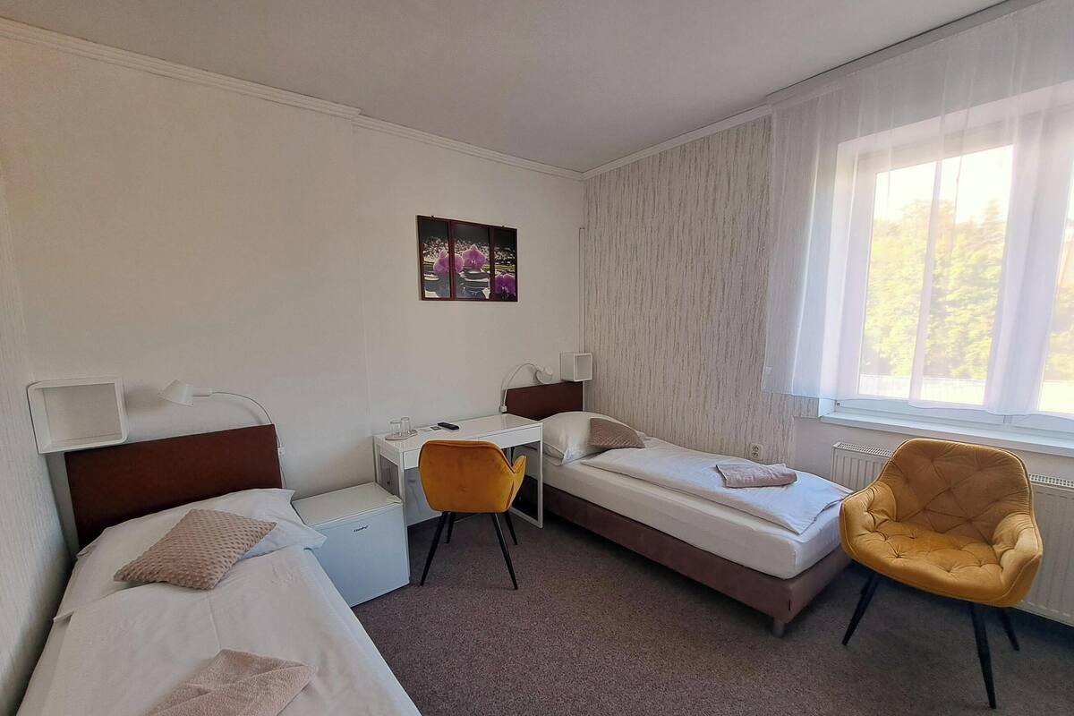 Et hotelværelse med to senge, et skrivebord, en stol, et vindue og et billede på væggen.