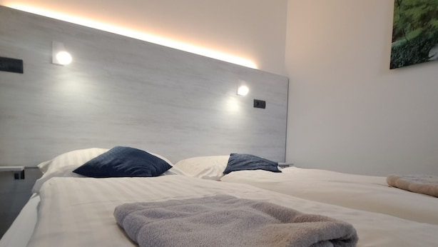 Moderni hotellihuone, jossa on suuri sänky, kaksi tyynyä, taitettu peitto ja seinään kiinnitetty valaisin.