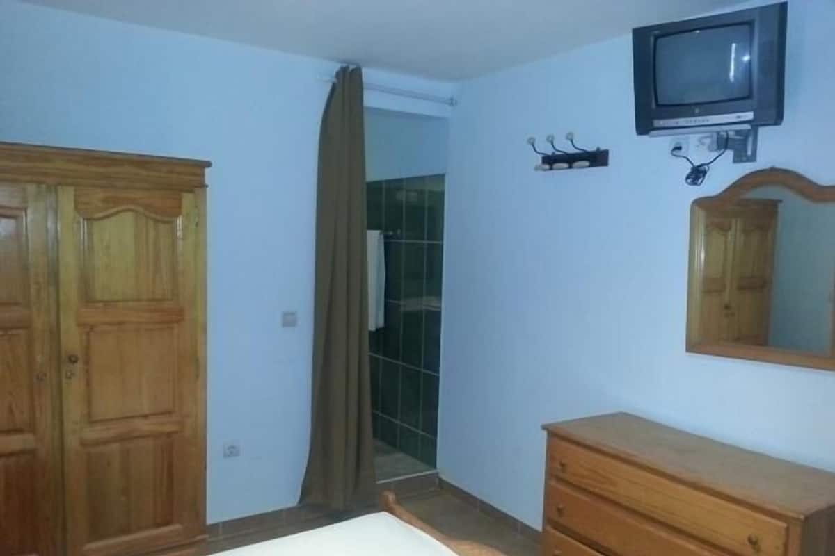 Ein Schlafzimmer mit Holzschrank, Schminktisch und einem an der Wand montierten Fernseher sowie einem Spiegel.