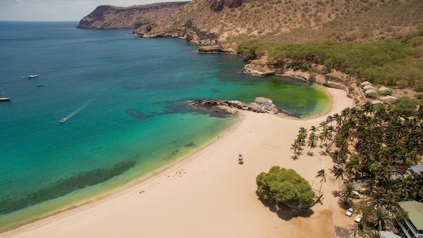A coastal beach with clear turquoise waters, a sandy shore, and a small boat anchored near the rocks. - Baia Verde (Tarrafal)