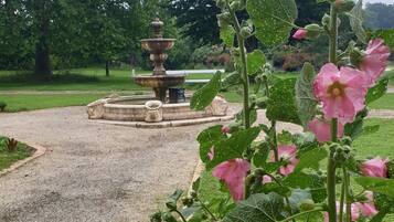 Un jardín con fuente, sendero de grava y plantas en flor.