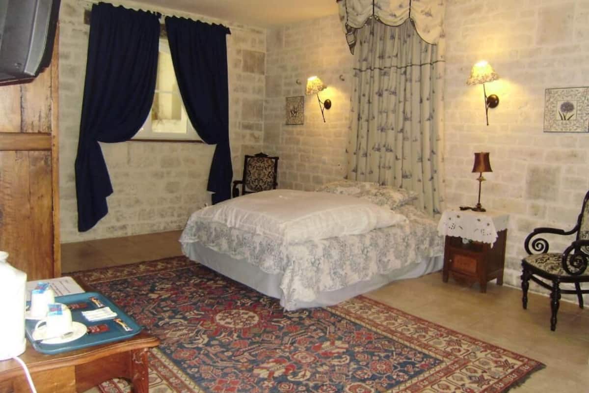 A bedroom with a bed, a rug, a chair, a table with a lamp, and a wall with a picture.