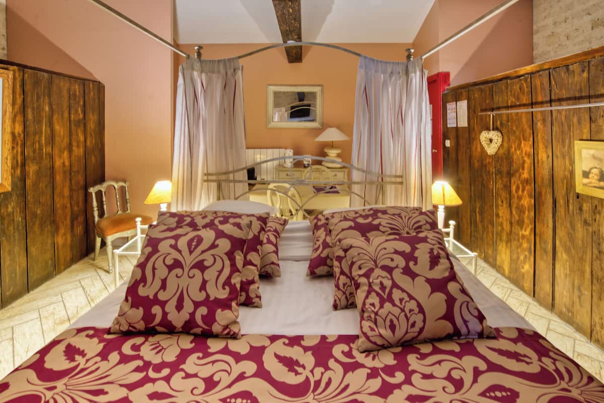A bedroom with a large bed, two bedside lamps, a wooden wardrobe, and a mirror on the wall.