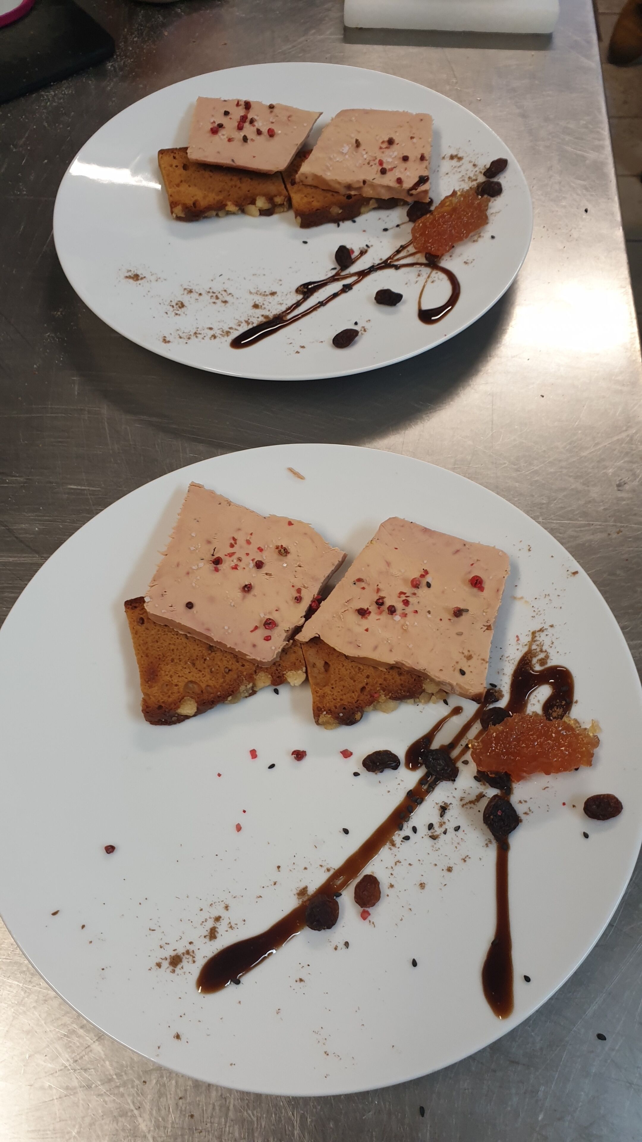 Two white plates with square-shaped desserts, each garnished with chocolate sauce and red berries.