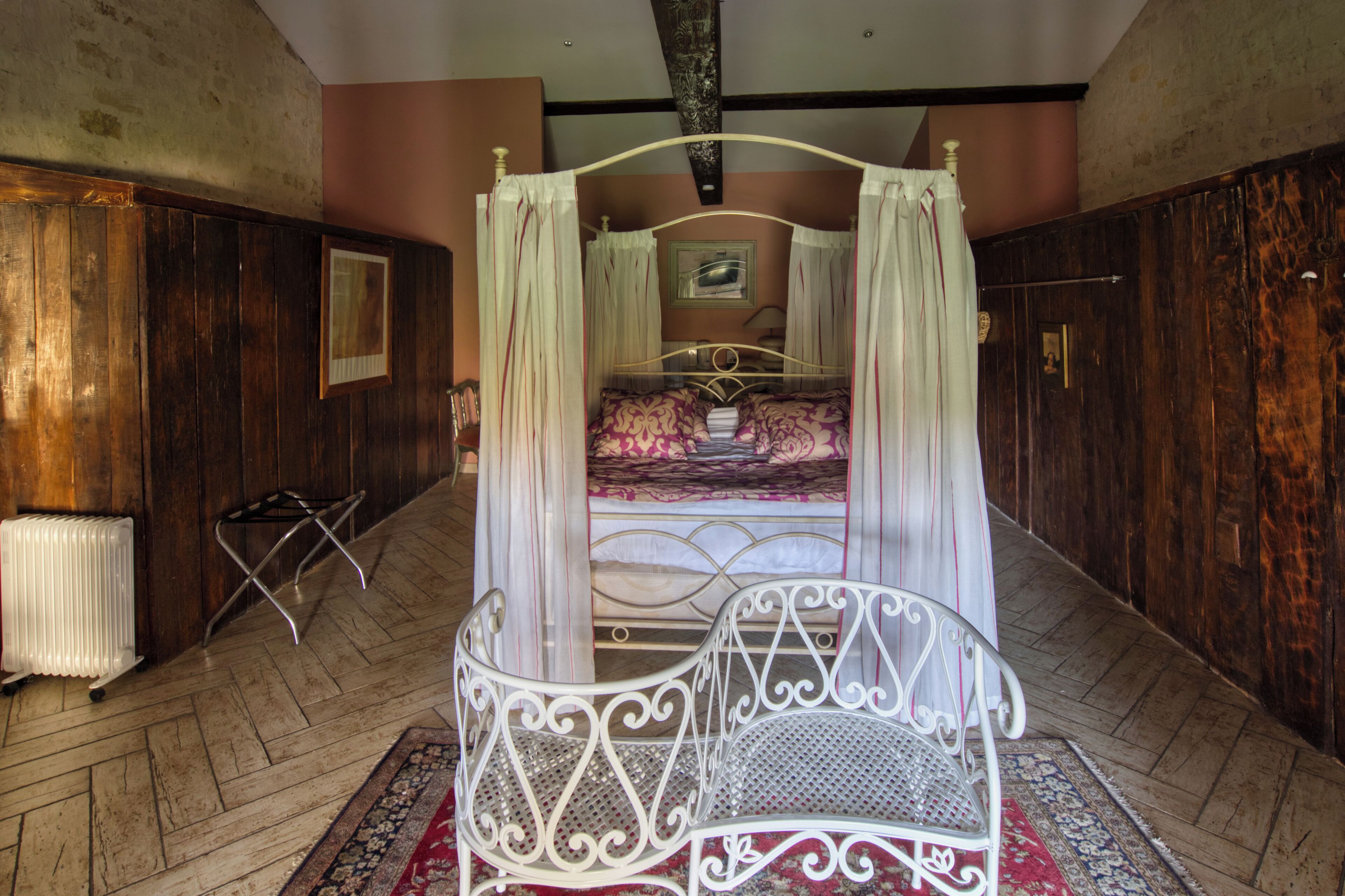 A four-poster canopy bed with a metal frame, a white radiator, and a patterned rug on a wooden floor.