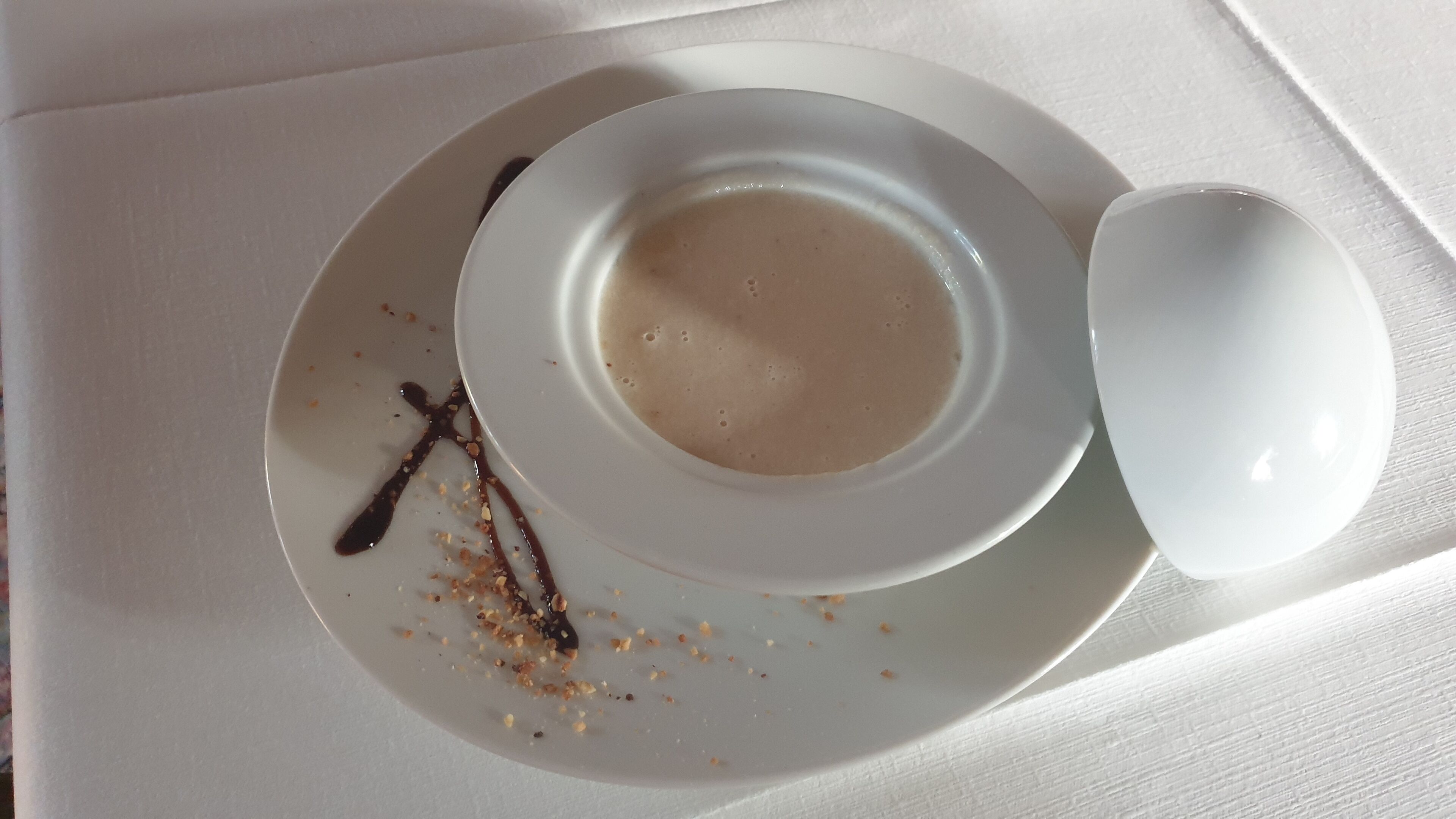 A white plate with a cup of coffee and a spoon, and a chocolate drizzle on the plate.