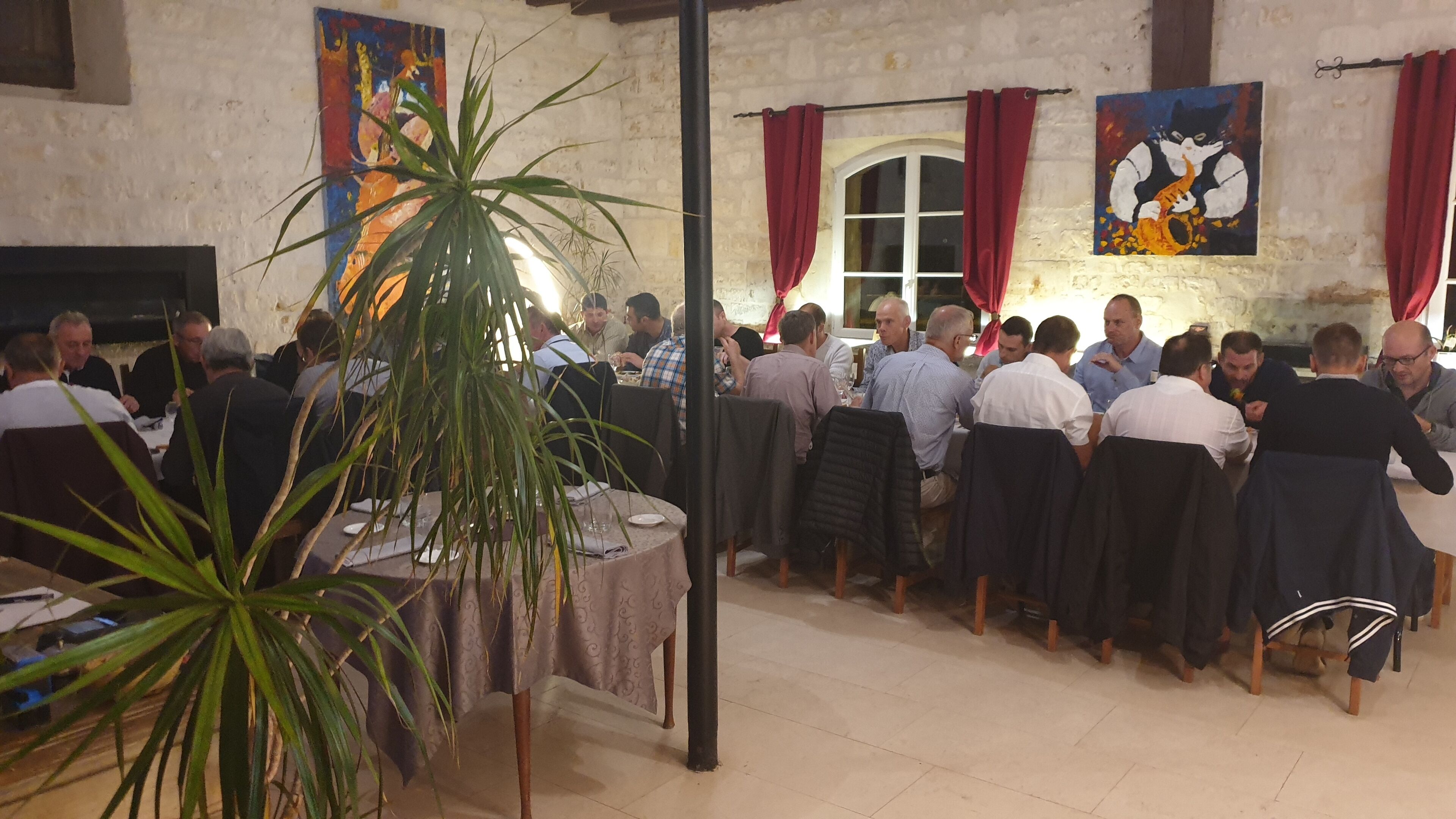 Un grupo de personas cenando en un espacio con pared de ladrillo rústica, una planta grande y obras de arte en las paredes.