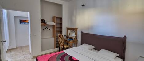Un dormitorio con cama, escritorio y silla. Hay una puerta que da a otra habitación.