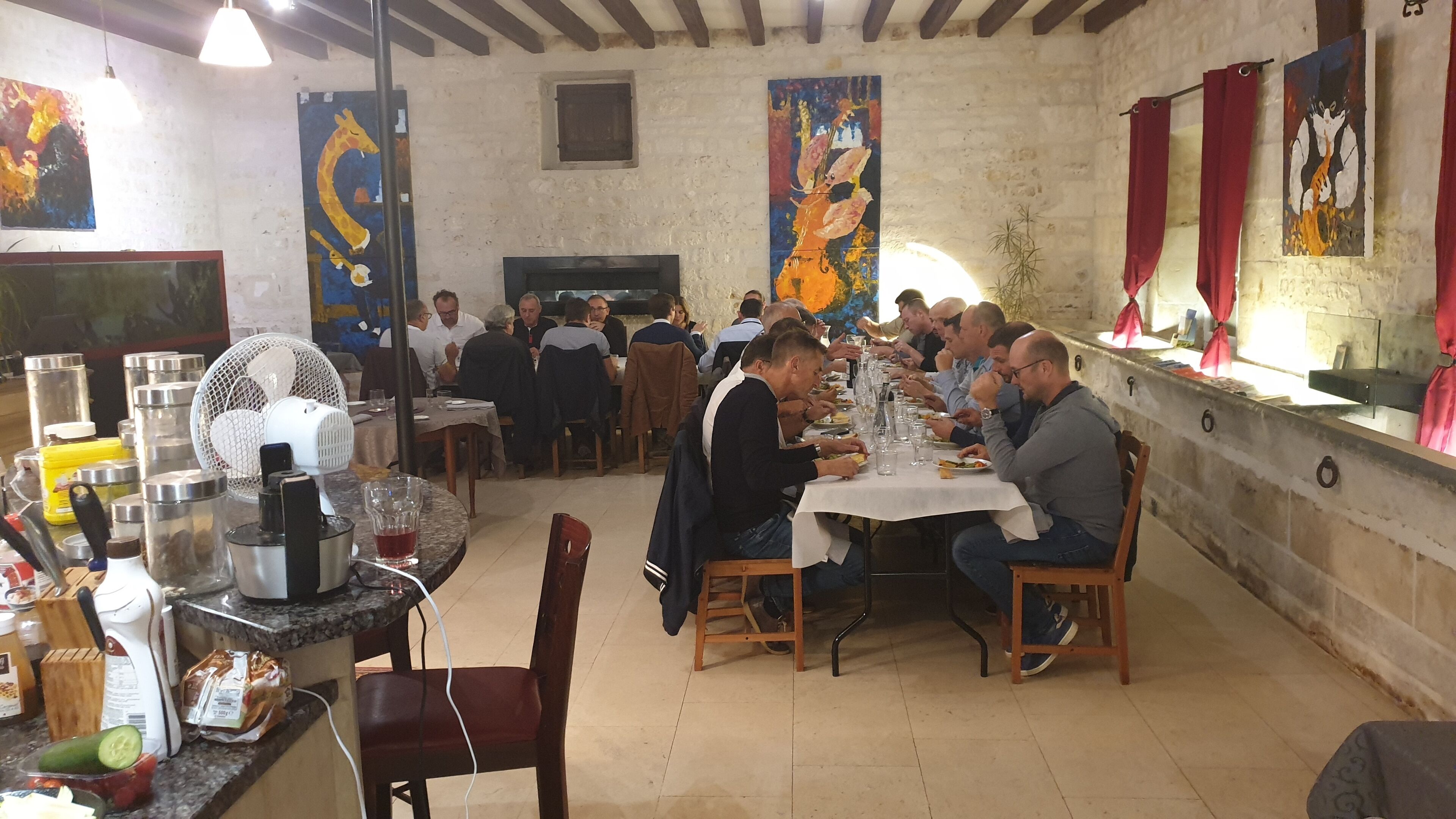 A restaurant with patrons dining at tables, a fan, and various kitchen items on the counter.