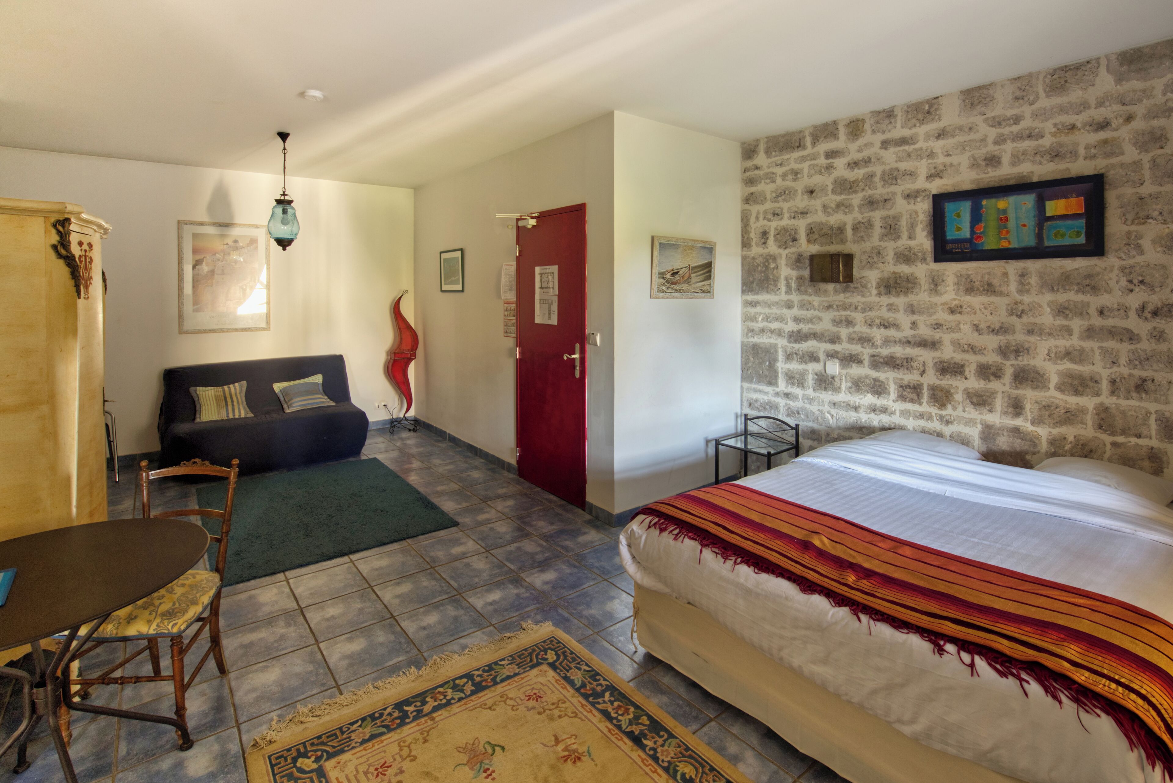 Une pièce comprenant un lit, un canapé, une table à manger et une chaise. Il y a une porte et un mur orné d’un cadre.