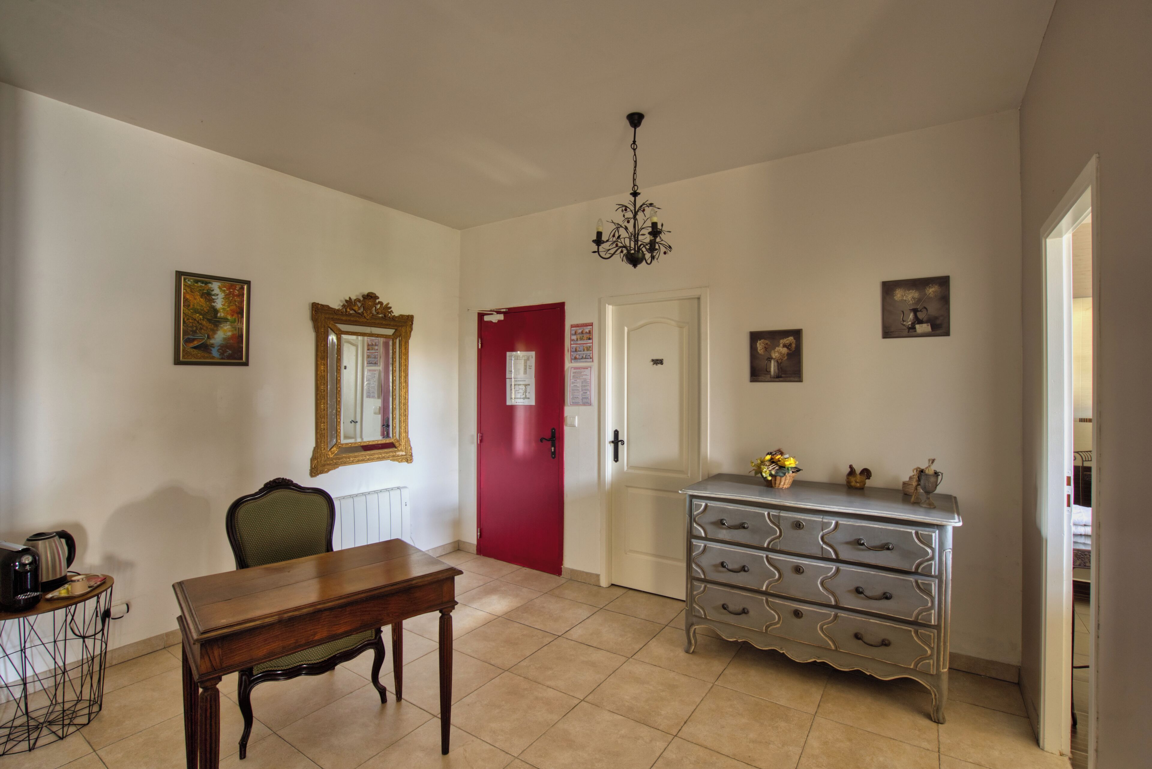 Una habitación con una mesa de madera, una puerta roja, un aparador y una araña.