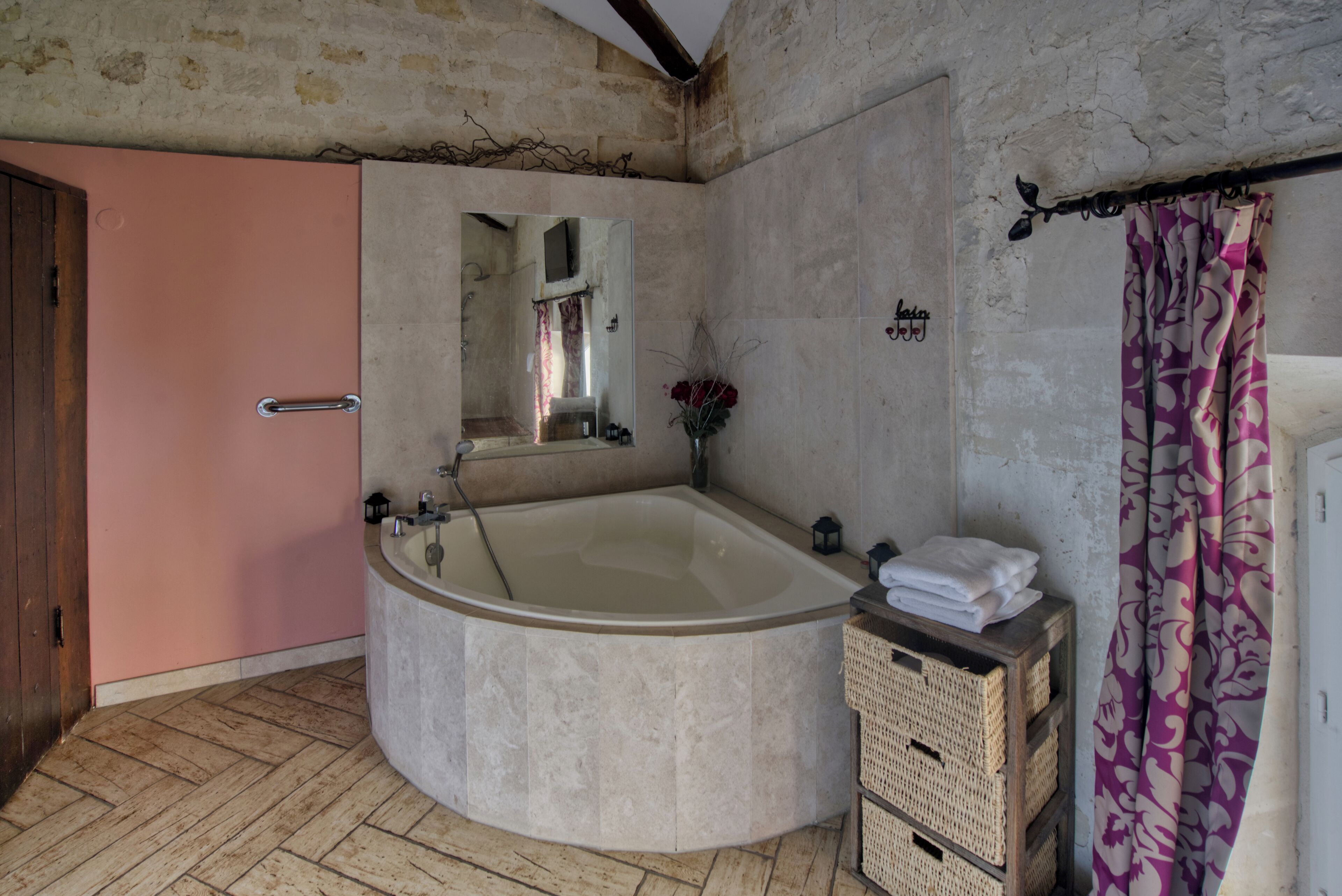 A bathroom with a large bathtub, a wooden door, a mirror, a towel rack, and a wicker basket.