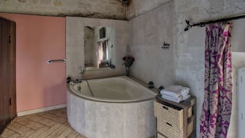 A bathroom with a large bathtub, a wooden door, a mirror, a towel rack, and a wicker basket.