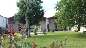 A courtyard with a building featuring a tiled roof, surrounded by trees and a well-maintained lawn. - Domaine des Chais (Thenac)