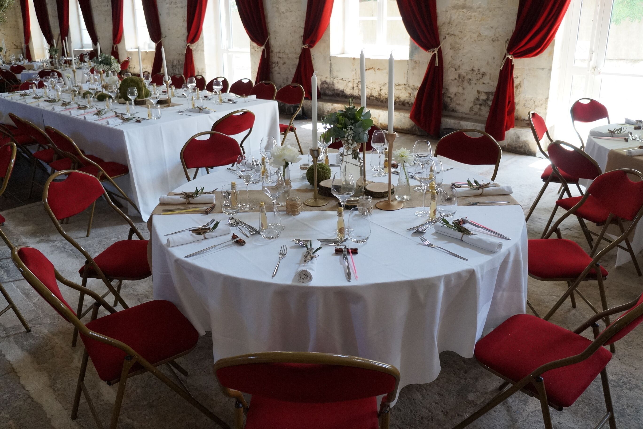 A banquet hall with round tables set for dining, red chairs, and white tablecloths.