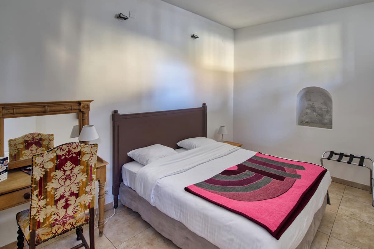 A bedroom with a bed, a chair, a lamp, and a small table.