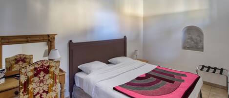 A bedroom with a bed, a chair, a lamp, and a small table.