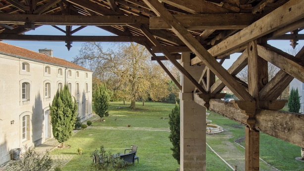 A courtyard with a wooden pergola, a building with multiple windows, and a well-maintained lawn. - Domaine des Chais (Thenac)