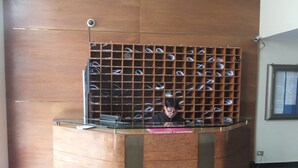 A reception desk with a person behind it, a shoe display wall, and a security camera on the wall. - Departamentos Centro Urbano Providencia (Santiago)