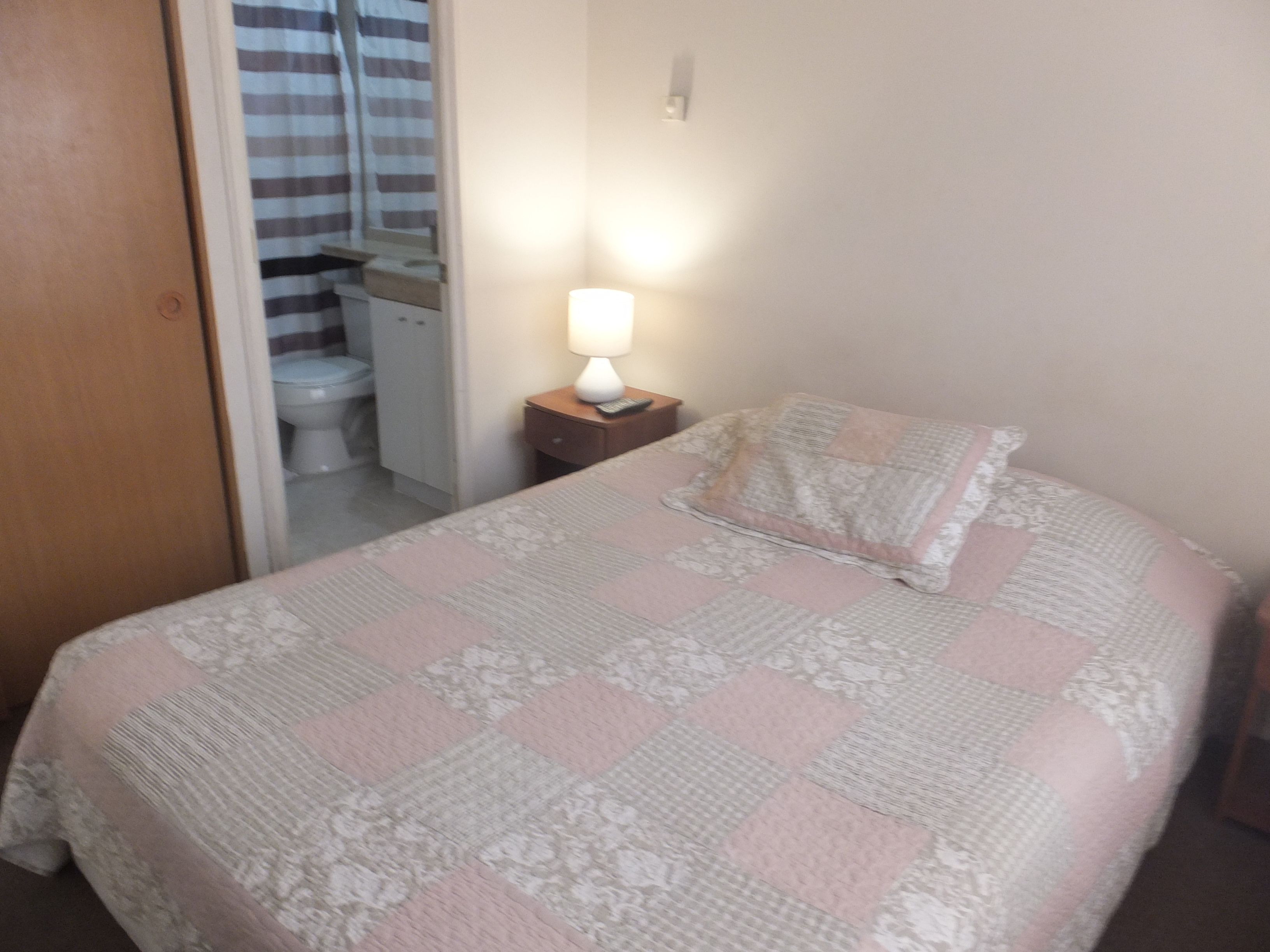 Une chambre à coucher comprenant un lit, une lampe de chevet, une table de chevet et une porte donnant sur une salle de bain.