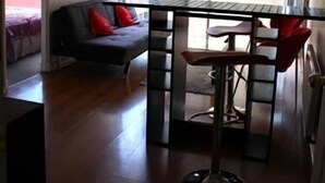 A modern living space with a glass dining table, a black sofa with red cushions, and a large window with sheer curtains. - Departamentos Centro Urbano Providencia (Santiago)