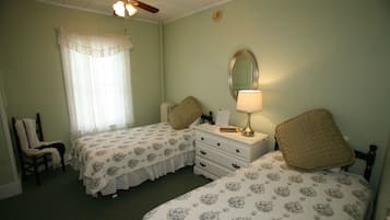 A bedroom with two beds, a ceiling fan, a window with curtains, a bedside table with a lamp, and a chair.
