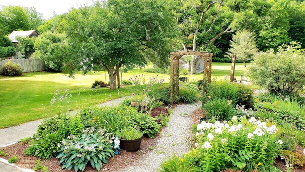 A well-maintained garden with a variety of plants and flowers, a wooden pergola, and a gravel path.