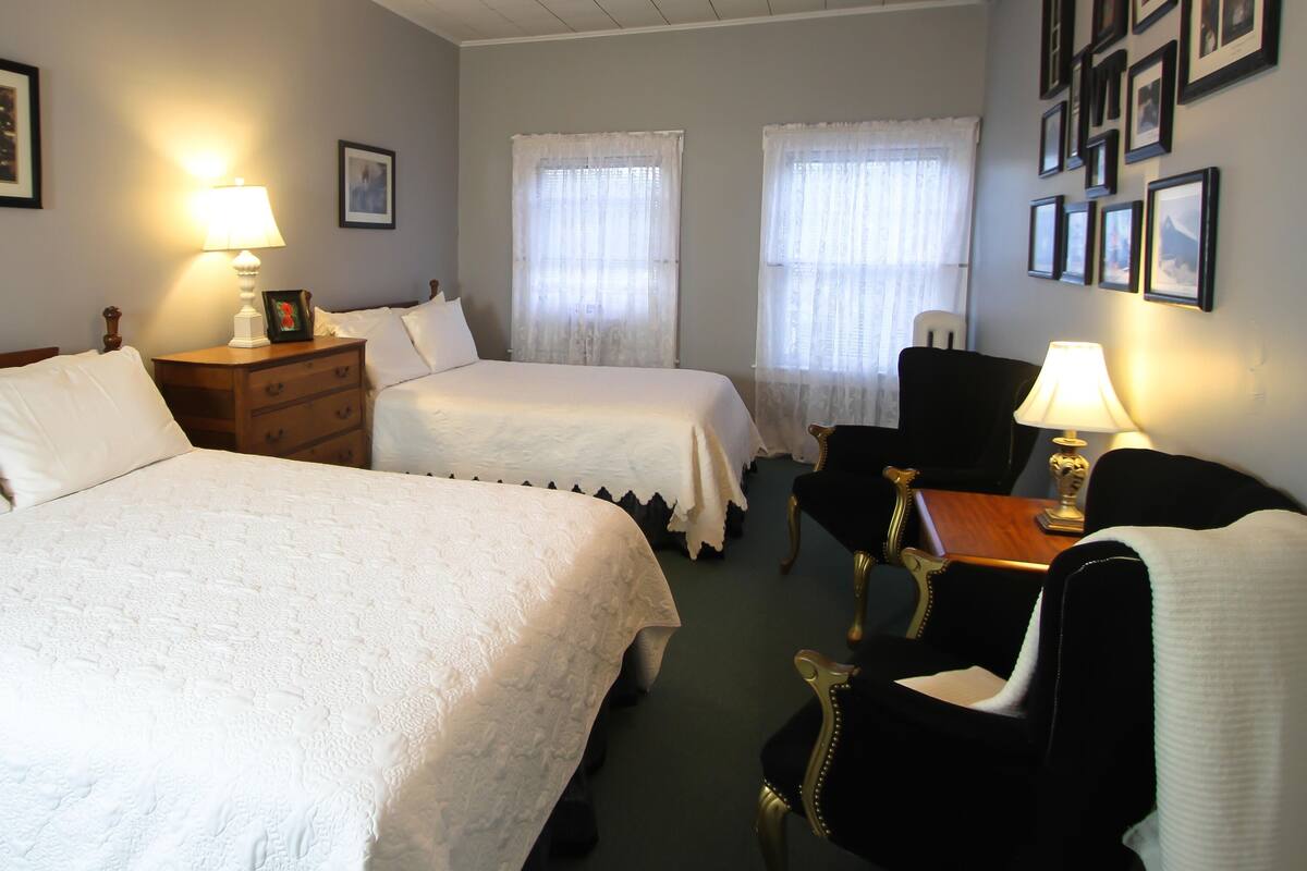 A hotel room with two beds, a desk, a chair, and a lamp.