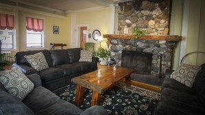 A cozy living room with a stone fireplace, a leather sofa set, a wooden coffee table, and a patterned rug.