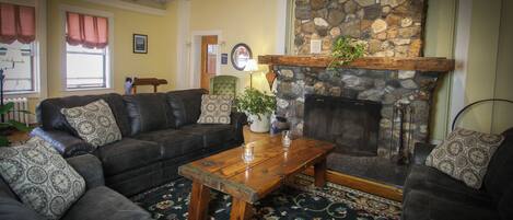 A cozy living room with a stone fireplace, a leather sofa set, a wooden coffee table, and a patterned rug.