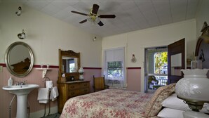 A bedroom with a bed, a bedside table, a lamp, a mirror, a dresser, a window, and a ceiling fan.