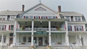A two-story building with a central entrance, a balcony with railings, and a sign indicating it is a lodging and fine dining establishment.