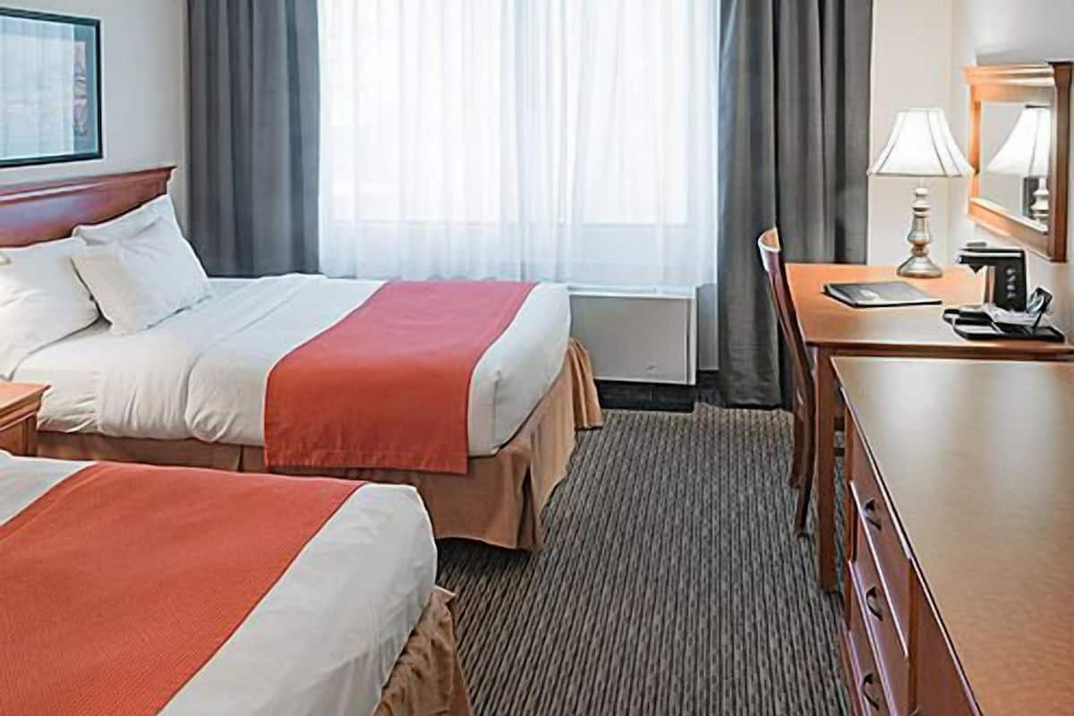 Habitación de hotel con dos camas, un escritorio, una silla, una lámpara y una ventana con cortinas.