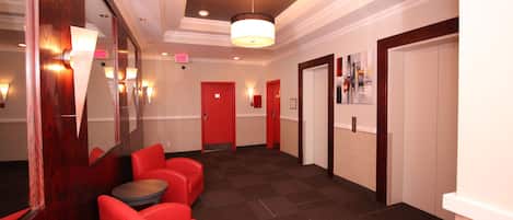 Un vestíbulo de hotel con asientos rojos, un espejo y un pasillo que conduce a puertas.