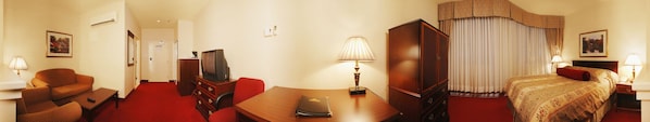 A hotel room with a red carpet, a sofa, a desk with a lamp, a television, a bed with a patterned bedspread, and a window with curtains. - Hotel Chrome Montreal (Montreal)