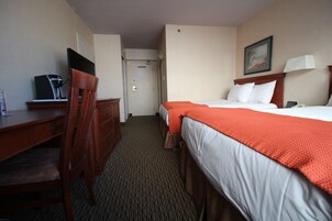 A hotel room with a bed, a desk, a chair, a television, and a door.